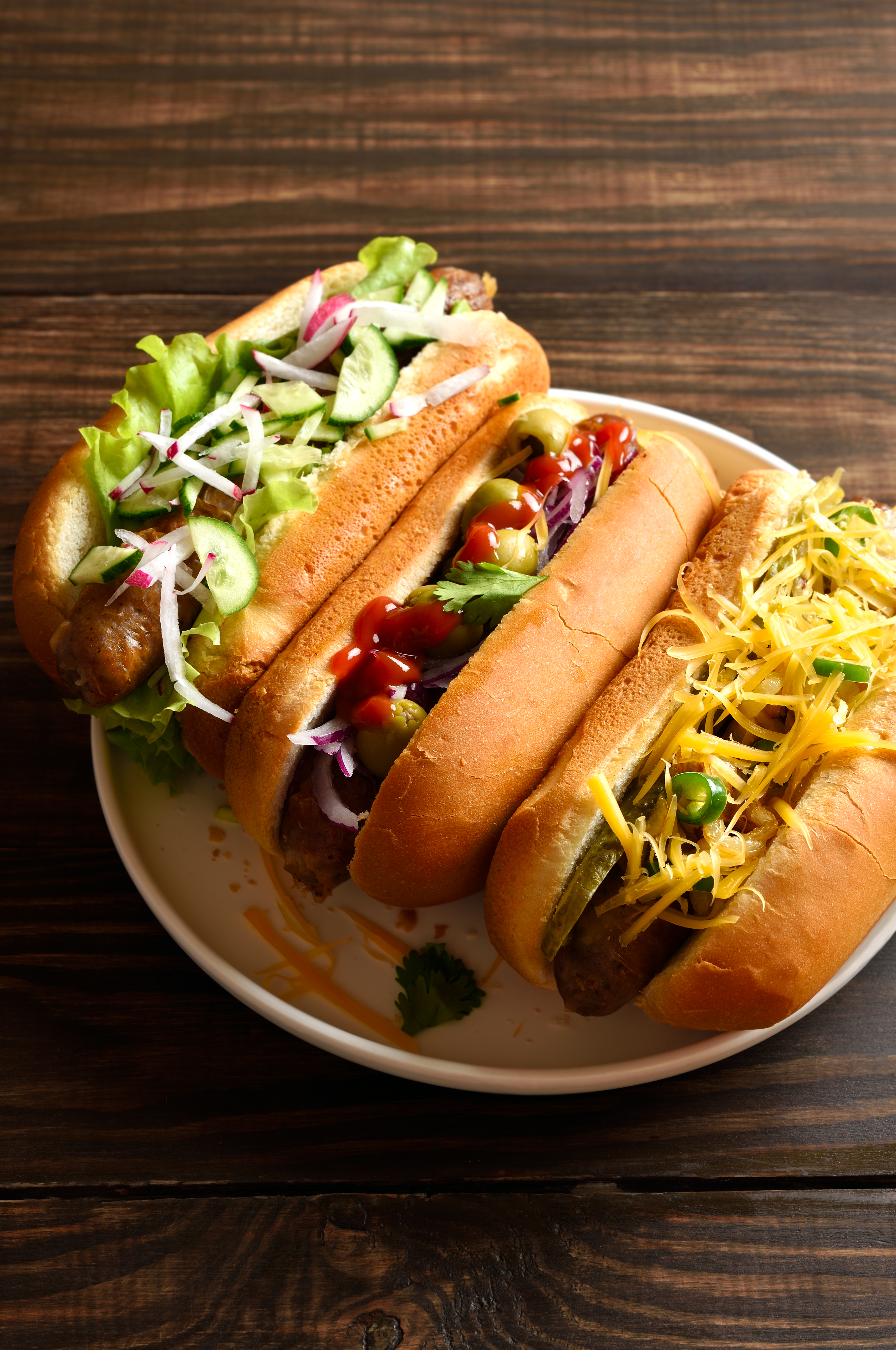 Hot dogs loaded with assorted toppings on wooden table. Close up view